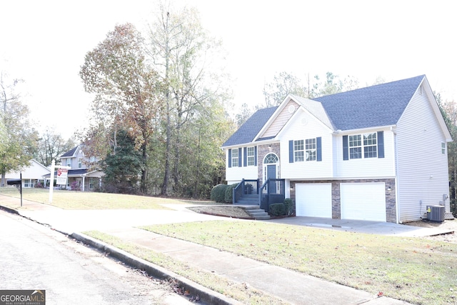 bi-level home featuring an attached garage, driveway, a front lawn, and central AC unit