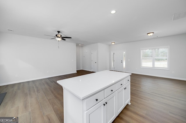 kitchen with white cabinets, ceiling fan, a kitchen island, and hardwood / wood-style flooring