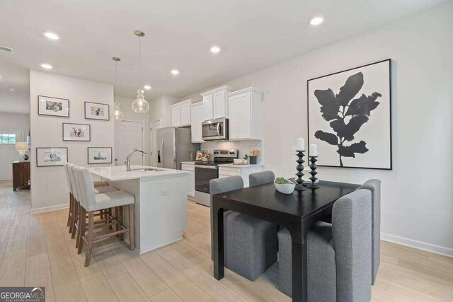 kitchen with appliances with stainless steel finishes, a kitchen island with sink, decorative light fixtures, light hardwood / wood-style flooring, and white cabinetry