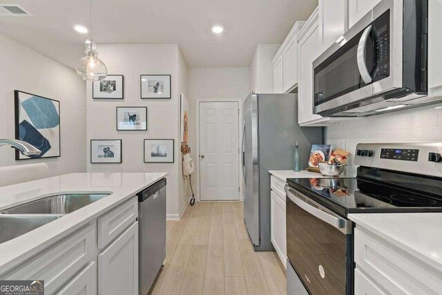 kitchen with white cabinets, sink, appliances with stainless steel finishes, decorative light fixtures, and light hardwood / wood-style floors