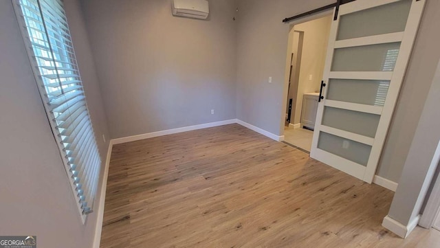 empty room with an AC wall unit, a barn door, built in shelves, and light hardwood / wood-style floors