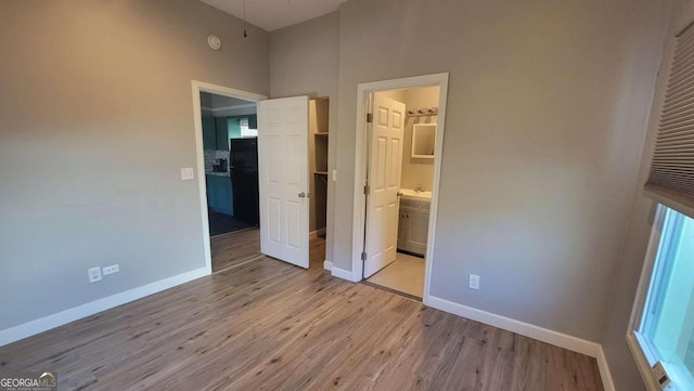 unfurnished bedroom featuring light hardwood / wood-style floors, black fridge, a high ceiling, and connected bathroom