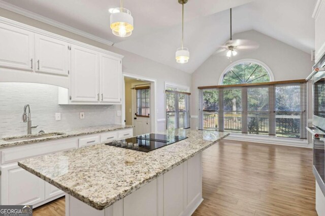 kitchen featuring stone countertops, appliances with stainless steel finishes, decorative light fixtures, a kitchen island, and white cabinetry