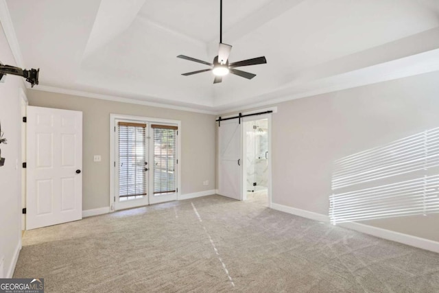 unfurnished bedroom featuring connected bathroom, ceiling fan, a barn door, a tray ceiling, and multiple windows