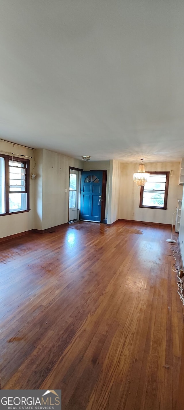 unfurnished living room with a healthy amount of sunlight, an inviting chandelier, and wood-type flooring