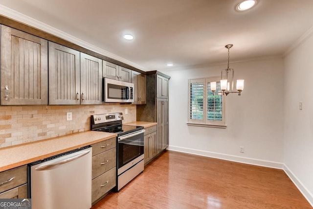 kitchen with appliances with stainless steel finishes, light wood-type flooring, crown molding, pendant lighting, and an inviting chandelier