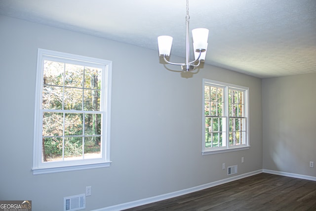 spare room with plenty of natural light, dark hardwood / wood-style floors, a textured ceiling, and an inviting chandelier