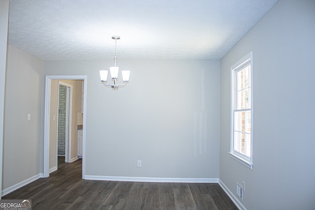 spare room featuring a chandelier, dark wood-type flooring, and a textured ceiling