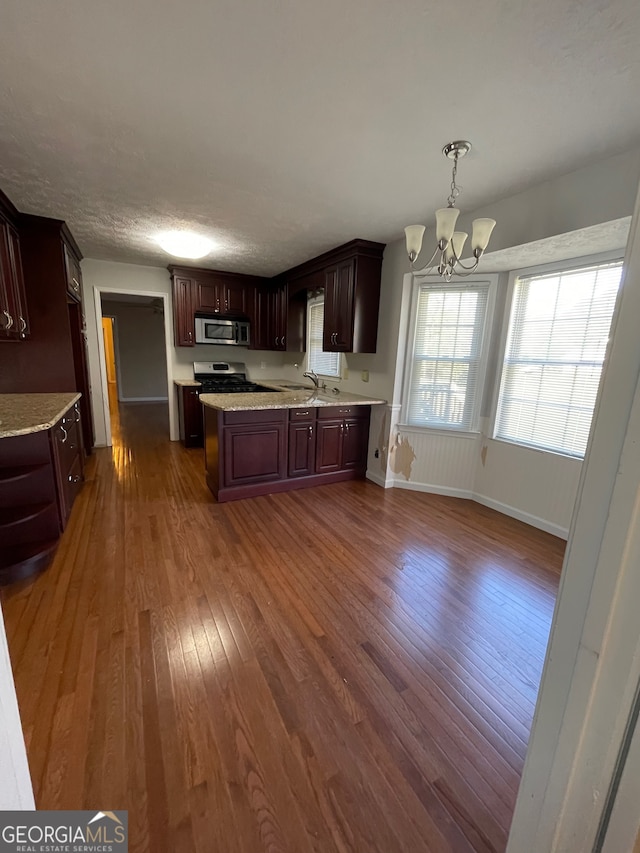 kitchen featuring appliances with stainless steel finishes, dark brown cabinets, pendant lighting, an inviting chandelier, and dark hardwood / wood-style floors