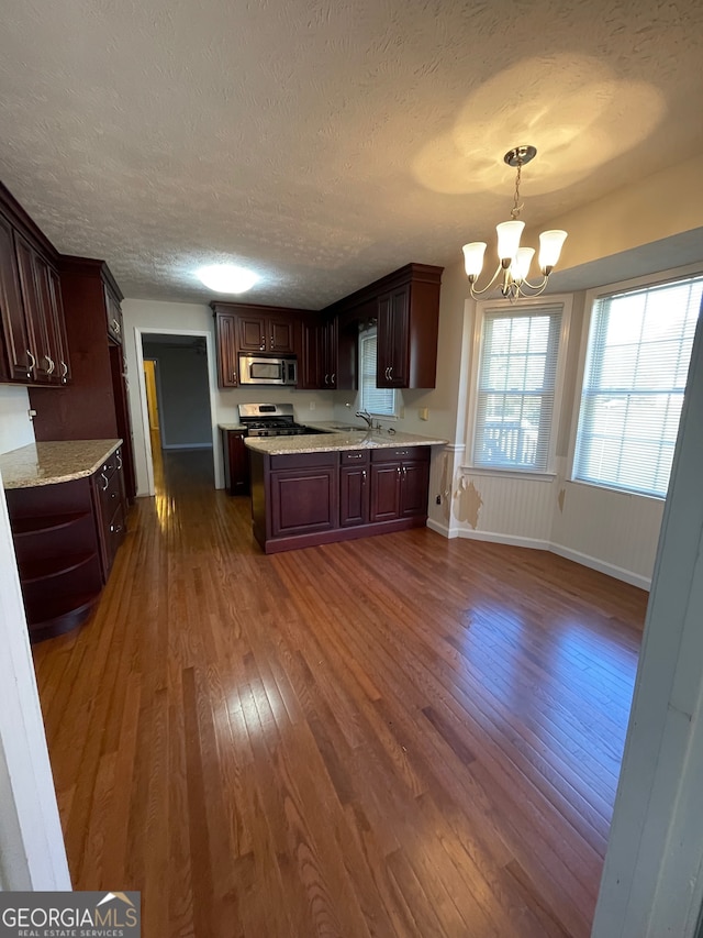 kitchen with appliances with stainless steel finishes, a textured ceiling, dark wood-type flooring, pendant lighting, and a notable chandelier