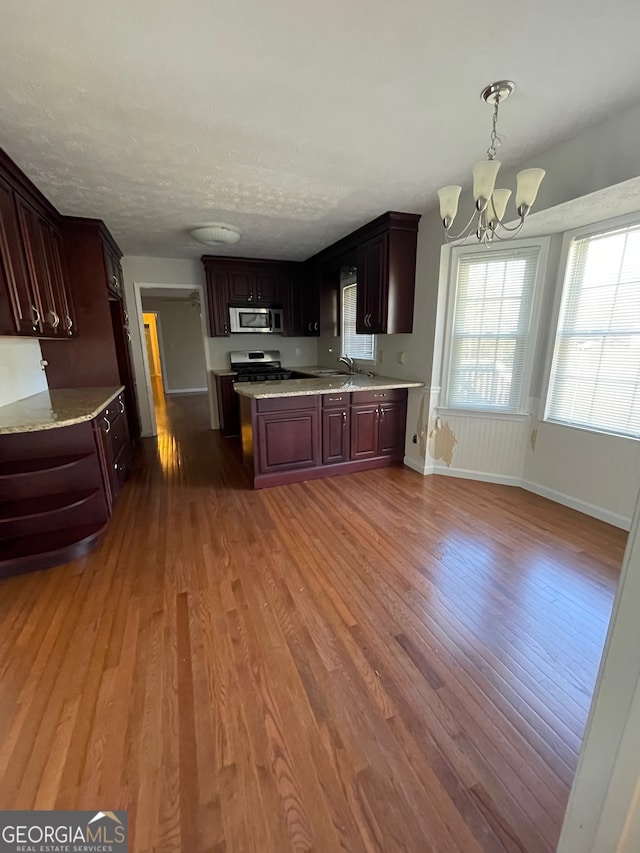 kitchen with appliances with stainless steel finishes, dark brown cabinetry, dark wood-type flooring, a notable chandelier, and hanging light fixtures