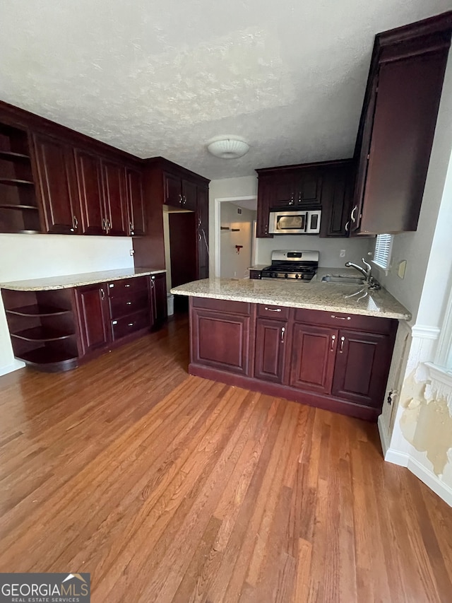 kitchen with light stone countertops, sink, light hardwood / wood-style floors, a textured ceiling, and appliances with stainless steel finishes