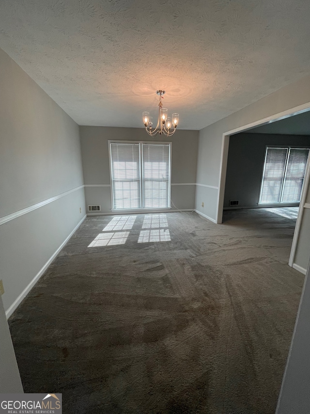 unfurnished room featuring carpet floors, a textured ceiling, and an inviting chandelier