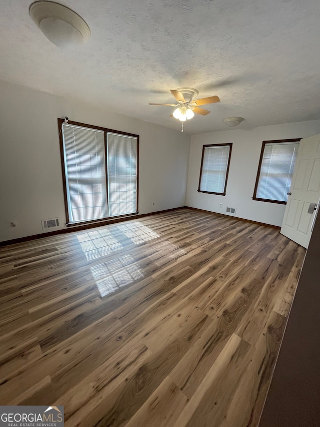 spare room featuring a textured ceiling, plenty of natural light, dark wood-type flooring, and ceiling fan