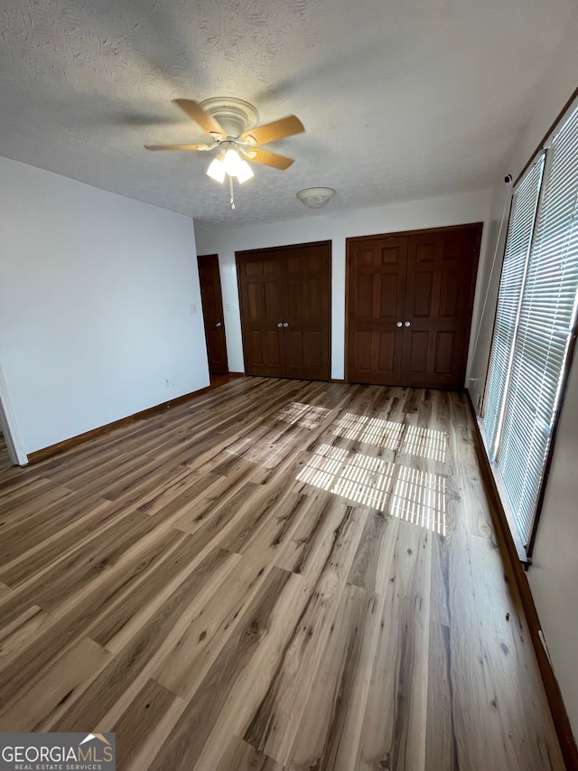 unfurnished bedroom with hardwood / wood-style floors, ceiling fan, a textured ceiling, and multiple closets