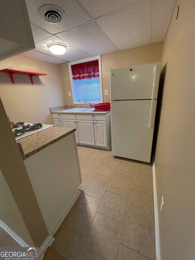 kitchen featuring white cabinetry, sink, white appliances, a paneled ceiling, and light tile patterned floors