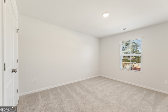 spare room featuring light colored carpet, visible vents, and baseboards