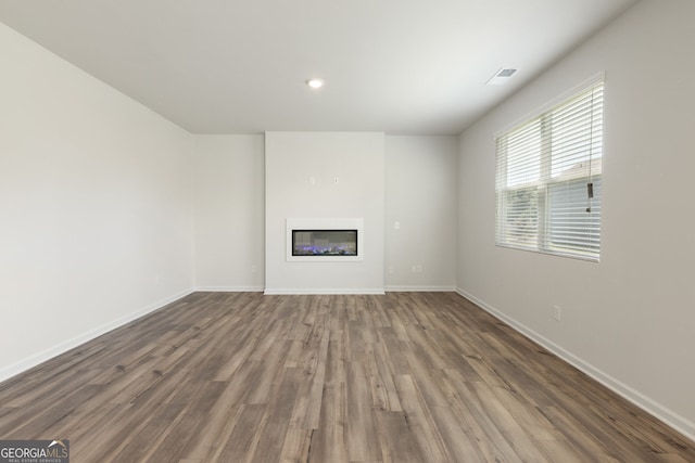 unfurnished living room featuring visible vents, baseboards, wood finished floors, and a glass covered fireplace