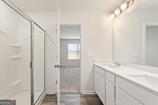 full bath with double vanity, wood finished floors, a stall shower, and a sink