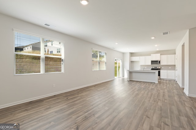 unfurnished living room with light wood-type flooring, visible vents, baseboards, and recessed lighting