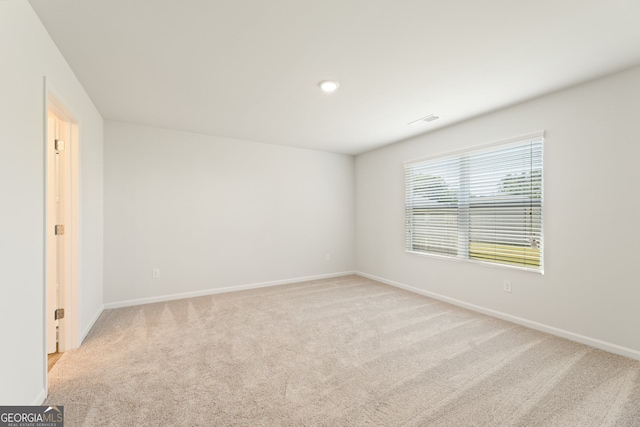 spare room featuring light colored carpet, visible vents, and baseboards