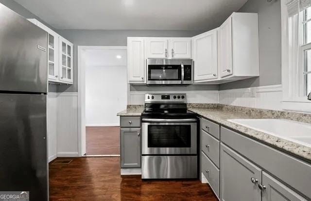 kitchen featuring sink, dark hardwood / wood-style floors, appliances with stainless steel finishes, light stone counters, and white cabinetry