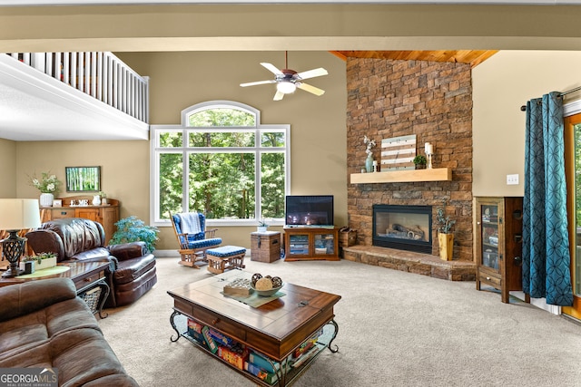 carpeted living room featuring beam ceiling, high vaulted ceiling, ceiling fan, and a stone fireplace