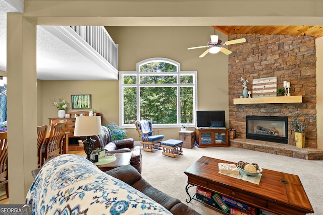 carpeted living room with beamed ceiling, high vaulted ceiling, a stone fireplace, and ceiling fan