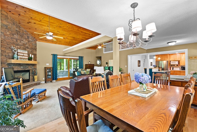 dining area with a textured ceiling, lofted ceiling, a fireplace, ceiling fan with notable chandelier, and light wood-type flooring