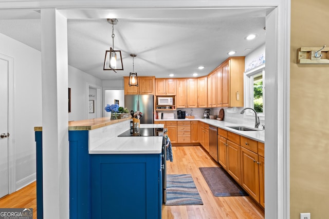 kitchen with sink, stainless steel appliances, pendant lighting, a textured ceiling, and light wood-type flooring