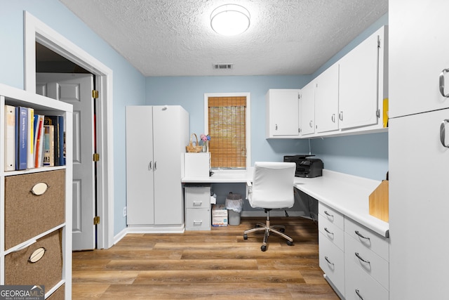 office area with built in desk, a textured ceiling, and light wood-type flooring