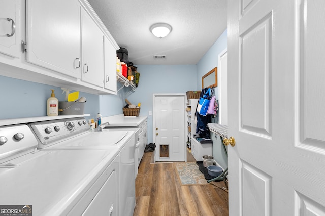 clothes washing area featuring washing machine and clothes dryer, dark wood-type flooring, cabinets, and a textured ceiling