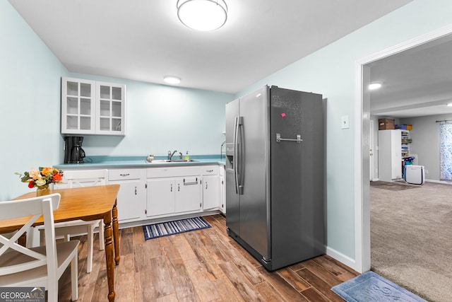 kitchen with stainless steel refrigerator with ice dispenser, hardwood / wood-style flooring, white cabinetry, and sink