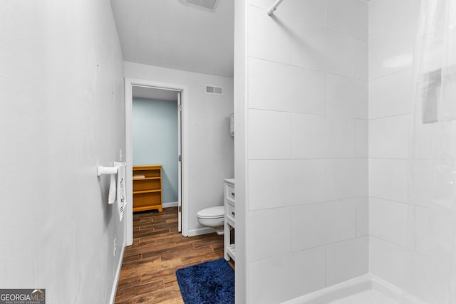 bathroom featuring toilet, hardwood / wood-style floors, vanity, and a tile shower