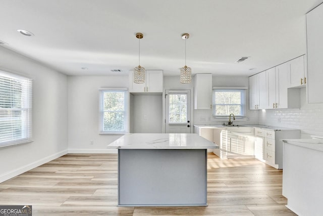 kitchen featuring decorative light fixtures, sink, white cabinets, decorative backsplash, and a center island