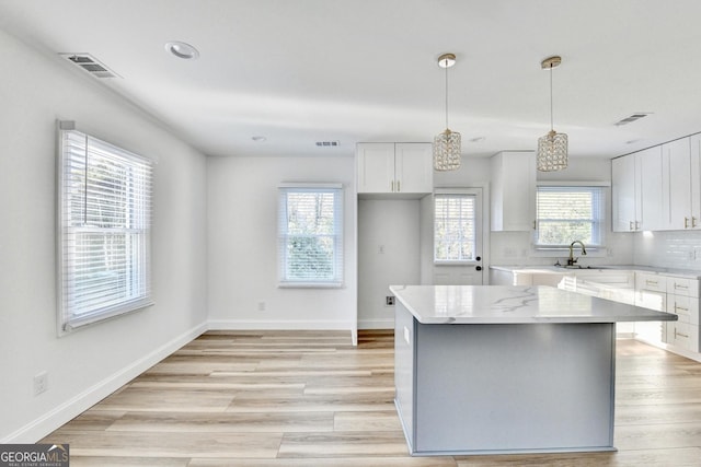 kitchen featuring a center island, hanging light fixtures, light stone countertops, decorative backsplash, and white cabinets