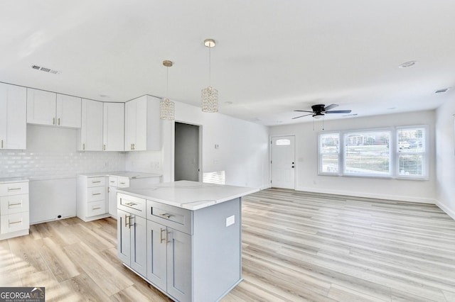 kitchen with backsplash, a center island, light stone countertops, white cabinets, and decorative light fixtures