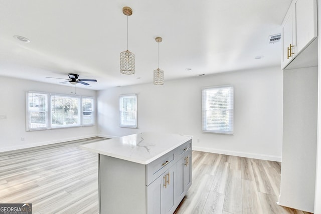 kitchen featuring pendant lighting, gray cabinets, light stone counters, white cabinets, and light wood-type flooring