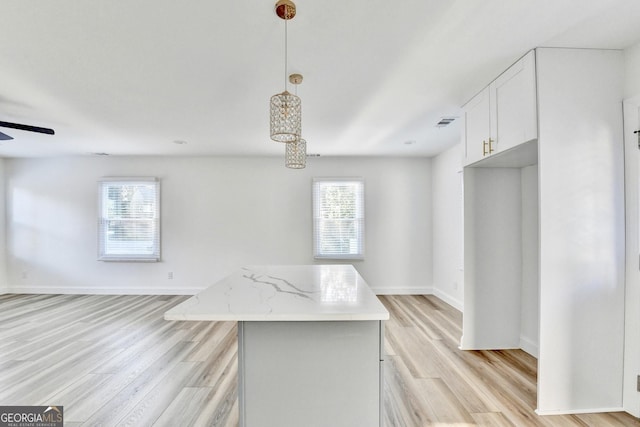 kitchen featuring light hardwood / wood-style flooring, hanging light fixtures, a center island, light stone counters, and white cabinets