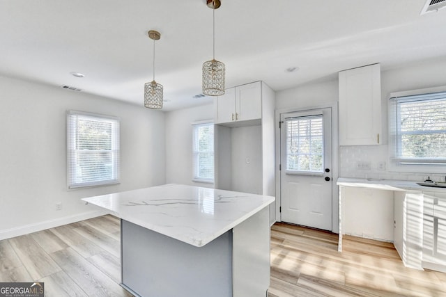 kitchen featuring pendant lighting, light hardwood / wood-style flooring, white cabinetry, a center island, and light stone countertops