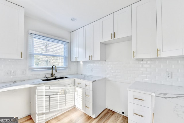 kitchen with white cabinetry, sink, backsplash, light stone countertops, and light wood-type flooring