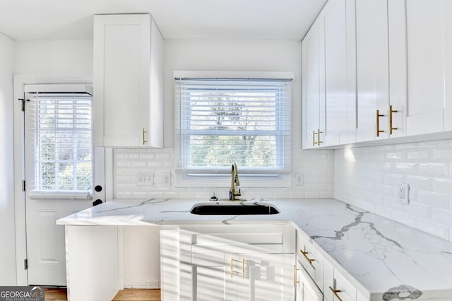 kitchen featuring white cabinetry, backsplash, light stone countertops, and sink