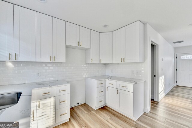 kitchen featuring white cabinetry, backsplash, light stone counters, and light wood-type flooring