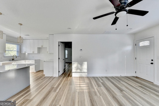 kitchen featuring pendant lighting, white cabinetry, sink, decorative backsplash, and light hardwood / wood-style floors