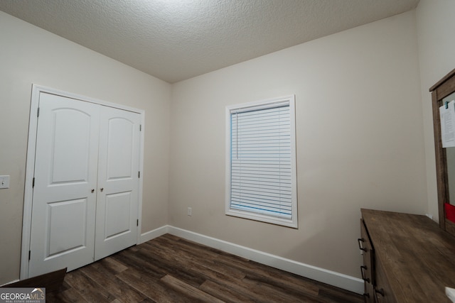 unfurnished bedroom featuring a textured ceiling, dark hardwood / wood-style floors, and a closet