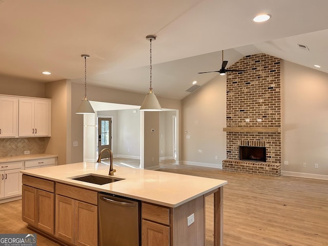 kitchen featuring decorative light fixtures, sink, white cabinets, stainless steel dishwasher, and a center island with sink