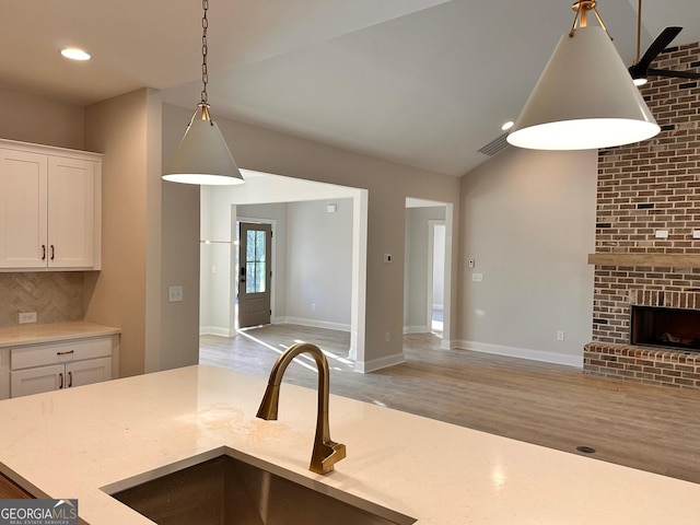 kitchen with vaulted ceiling, pendant lighting, a fireplace, white cabinetry, and sink