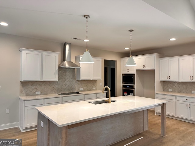 kitchen with white cabinetry, pendant lighting, a kitchen island with sink, and wall chimney range hood