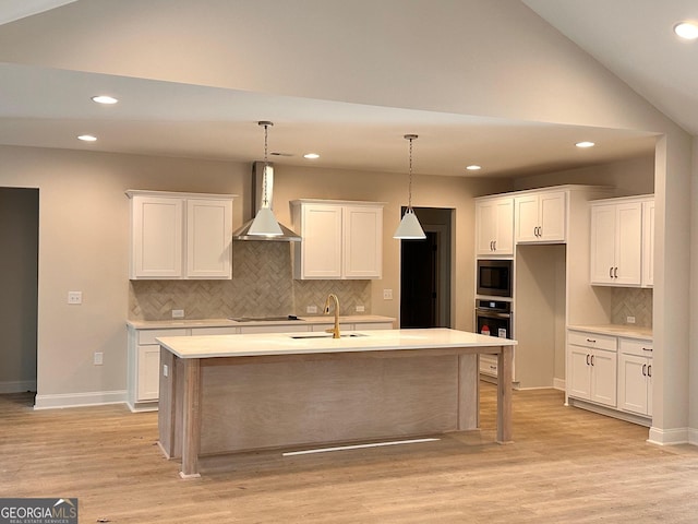 kitchen with a kitchen island with sink, wall chimney range hood, and white cabinets