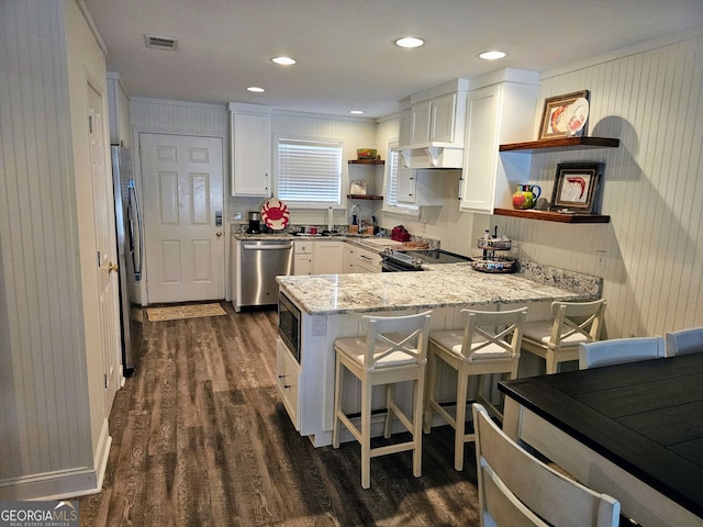 kitchen featuring kitchen peninsula, light stone countertops, a breakfast bar, stainless steel appliances, and white cabinets